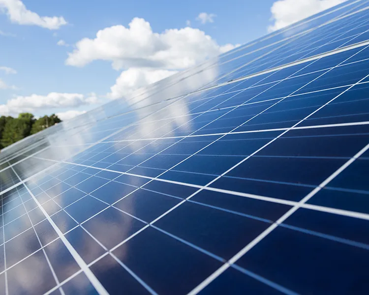 Paneles solares fotovoltaicos con cielo nublado y sol entre nubes.