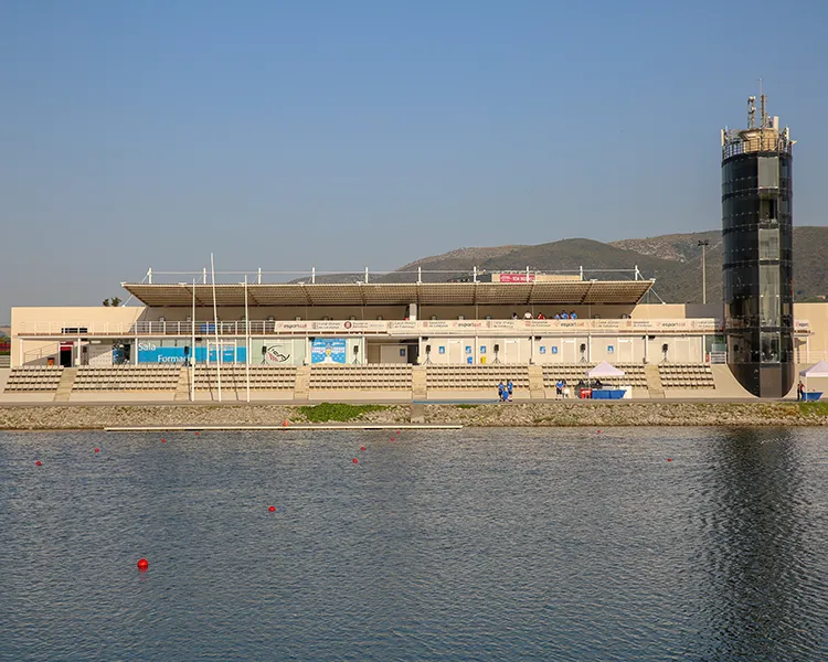 Estadio costero con torre de control junto al mar y luces al atardecer