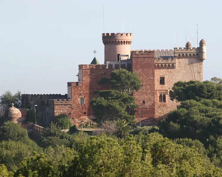 Castillo de ladrillo con torres y &aacute;rboles alrededor, bajo el cielo azul