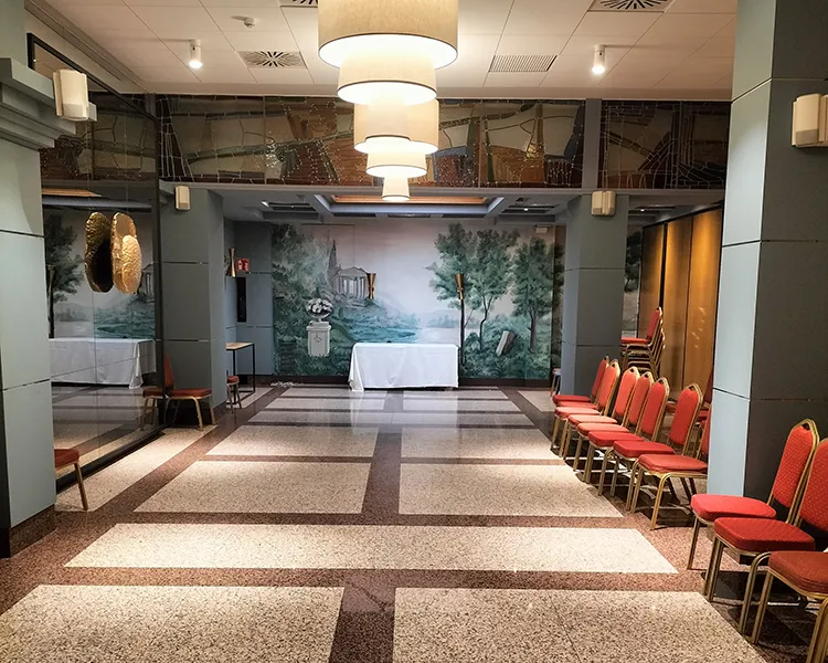 Sala de hotel con alfombra, sillas rojas y mural de bosque en el fondo.