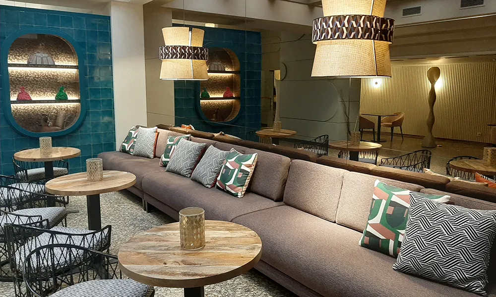 Sala lounge con sof&aacute; gris, mesas de madera y l&aacute;mparas colgantes decorativas