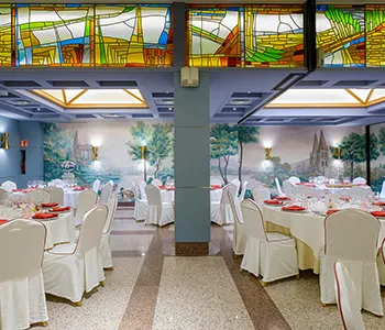 Sal&oacute;n de banquetes con mesas y sillas, luces y decoraci&oacute;n colorida al fondo
