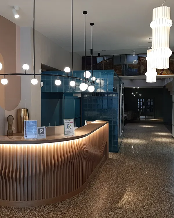 Recepci&oacute;n moderna con mostrador de madera, azulejos y l&aacute;mparas colgantes blancas.