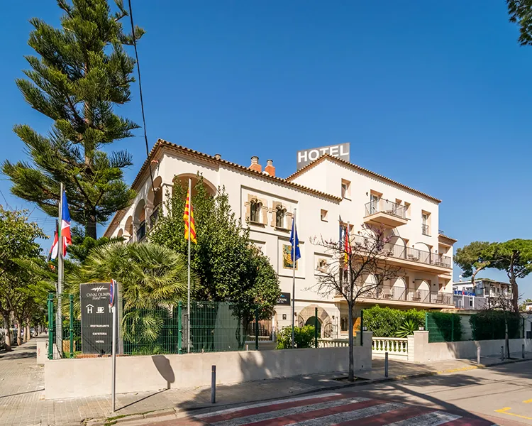 Fachada de hotel con bandera, &aacute;rboles y jard&iacute;n bajo cielo azul