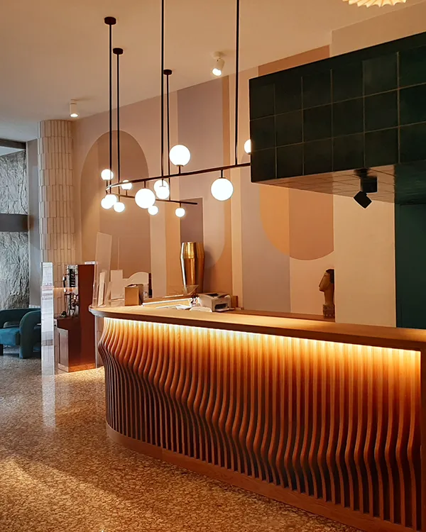 Recepci&oacute;n con mostrador de madera, luces colgantes y pared verde oscura.