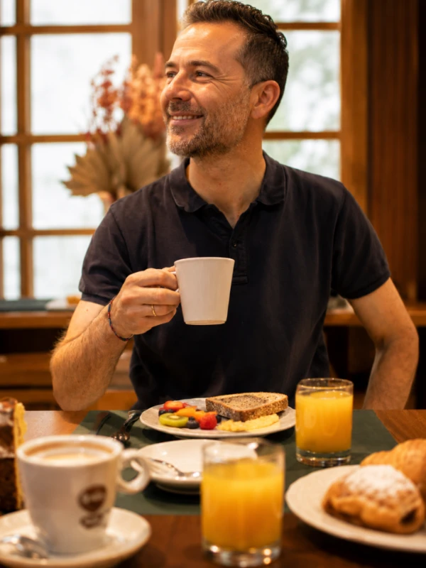 Hombre sonriendo con taza de caf&eacute; en un desayuno junto a un plato