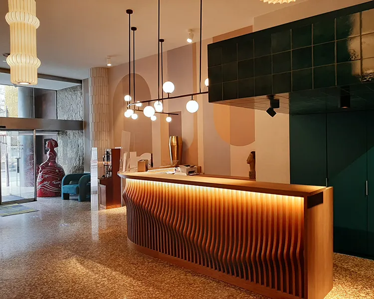 Recepci&oacute;n moderna con mostrador de madera y l&aacute;mparas colgantes en hotel.