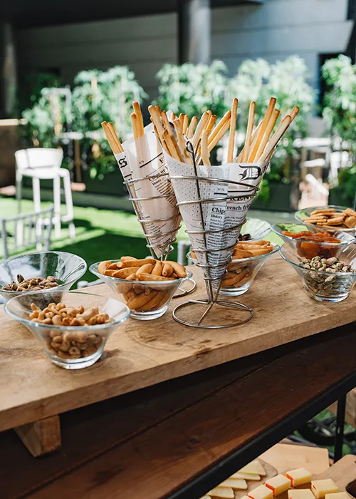 Mesa con snacks y recipientes con palitos de pan en un evento al aire libre.