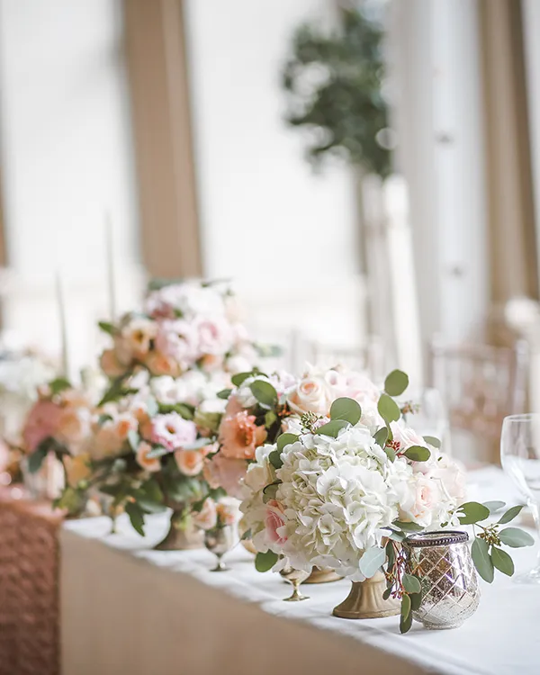 Mesa decorada con arreglos florales blancos y rosados, en un evento.