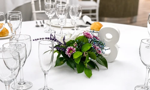 Centro floral morado en mesa con copas y decoraciones para banquete