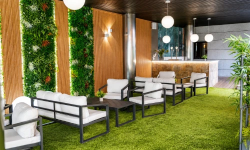 Patio moderno con c&eacute;sped artificial, bancos y paredes decoradas con plantas.