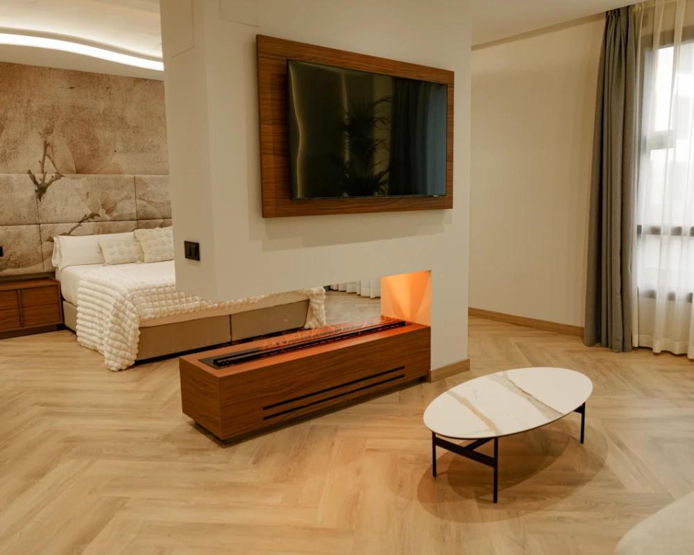 Sala moderna con cama, TV, chimenea y mesa oval con l&aacute;mpara de pared.