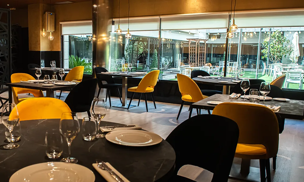 Sal&oacute;n de restaurante con mesas servidas y sillas amarillas, luz c&aacute;lida.