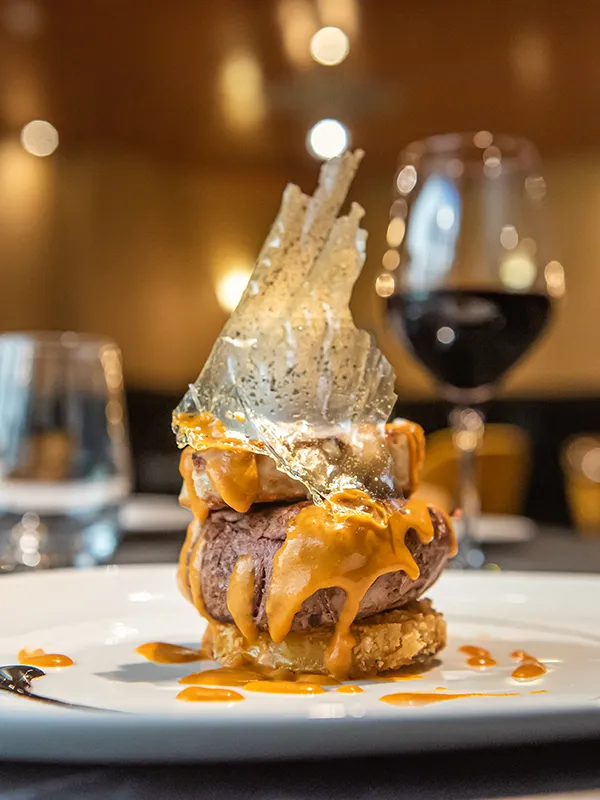 Postre con base de carne y salsa, con cono de az&uacute;car sobre plato blanco.