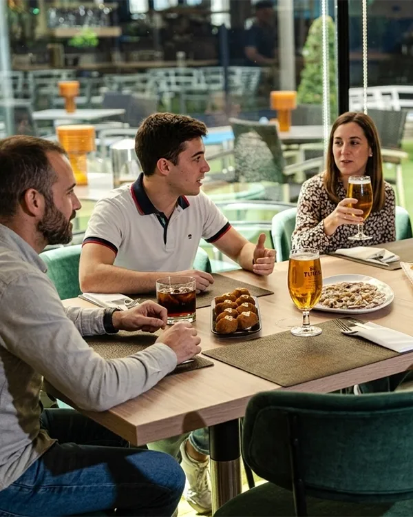 Tres personas brindan en una mesa en un restaurante con platos y cerveza