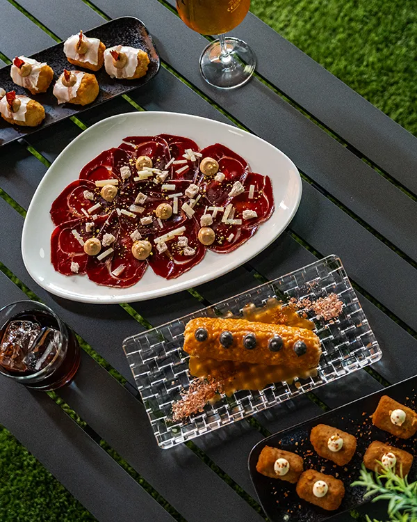 Plato de ravioles con salsa roja y aperitivos en mesa al aire libre