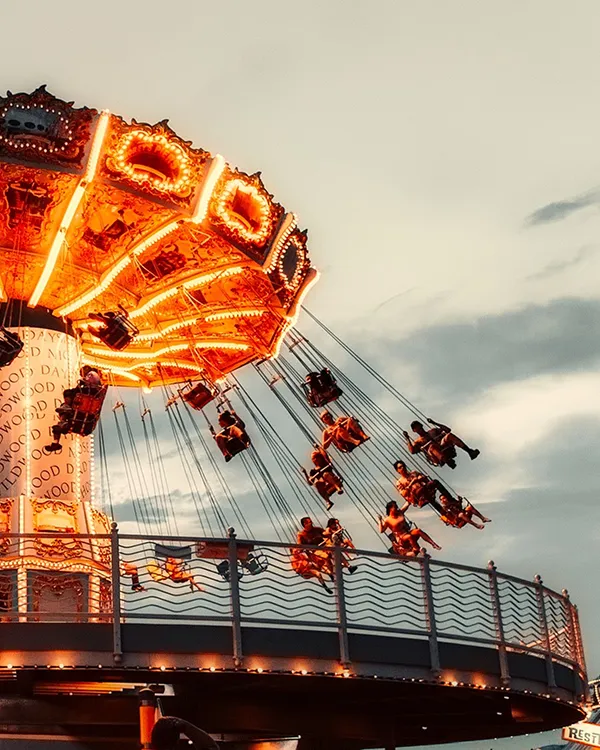 Rueda de feria iluminada con coches y luces naranjas en el cielo