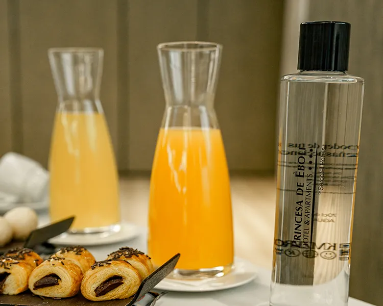 Botella de perfume y bebidas naranjas con bollitos sobre mesa