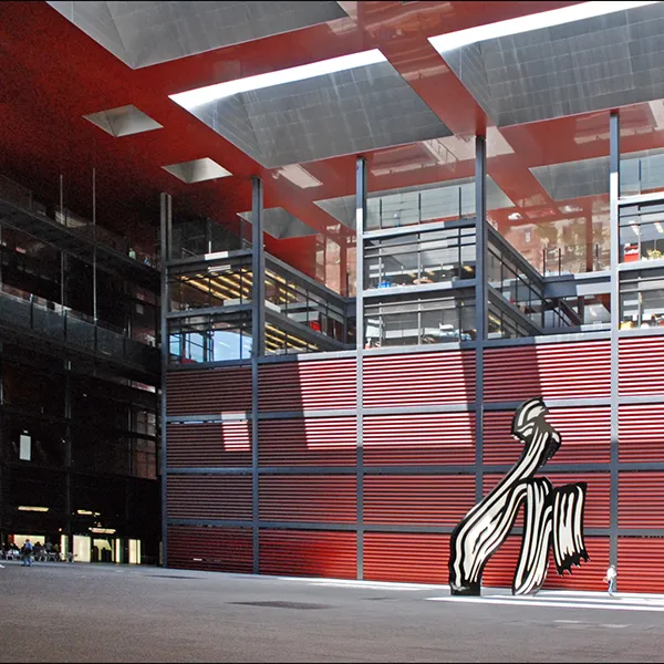 Interior de estadio con gradas, paneles rojos y mural de mujer.