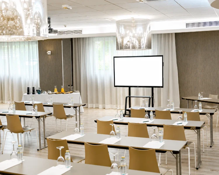Sala de reuniones con mesas, sillas y proyector en el centro.