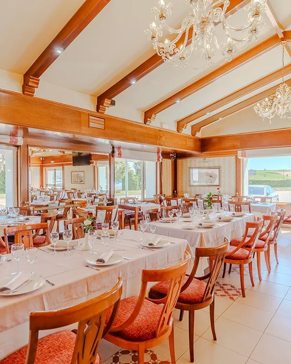 Comedor elegante con mesas servidas y ara&ntilde;a de cristal en sal&oacute;n luminoso.
