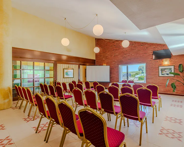 Sala de conferencias con filas de sillas rojas y blancas y pared de ladrillo