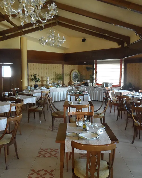 Comedor de hotel con mesas servidas, sillas de madera y l&aacute;mparas de cristal.