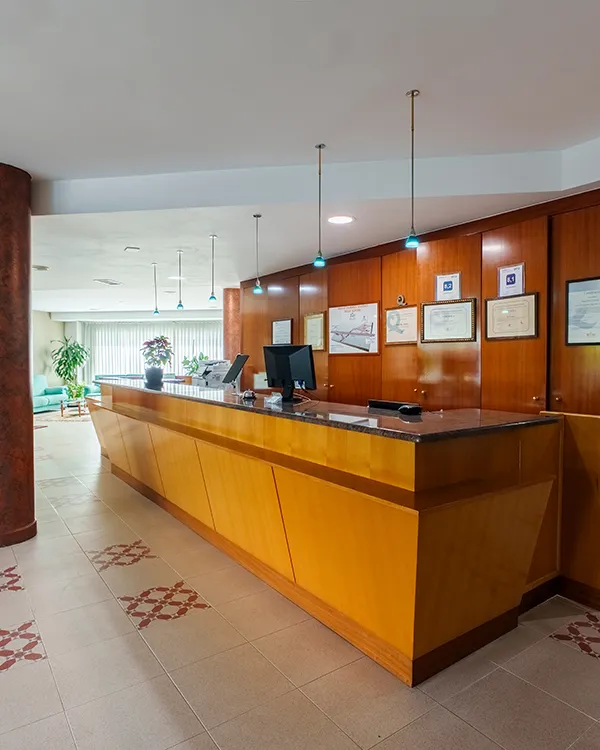 Recepci&oacute;n de hotel con mostrador de madera, pantallas y diplomas en la pared