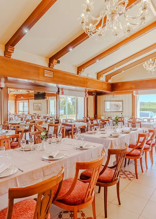 Comedor elegante con mesas servidas, sillas de madera y ara&ntilde;as de luz.