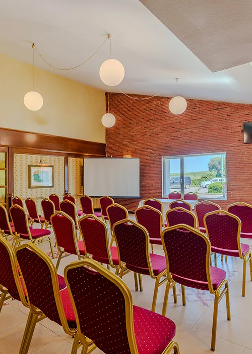 Sala de conferencias con sillas rojas y paredes de ladrillo.