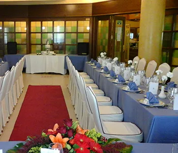 Sal&oacute;n de eventos con mesas, sillas y decoraci&oacute;n floral en el centro.