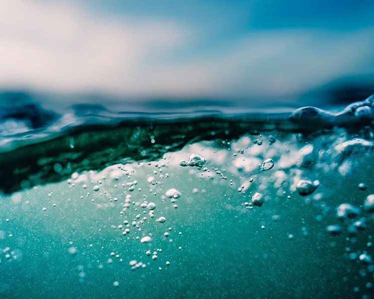 Olas azules con burbujas y gotas de agua en primer plano.