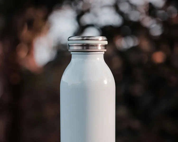 Botella de bebida blanca con tapa met&aacute;lica, fondo desenfocado.