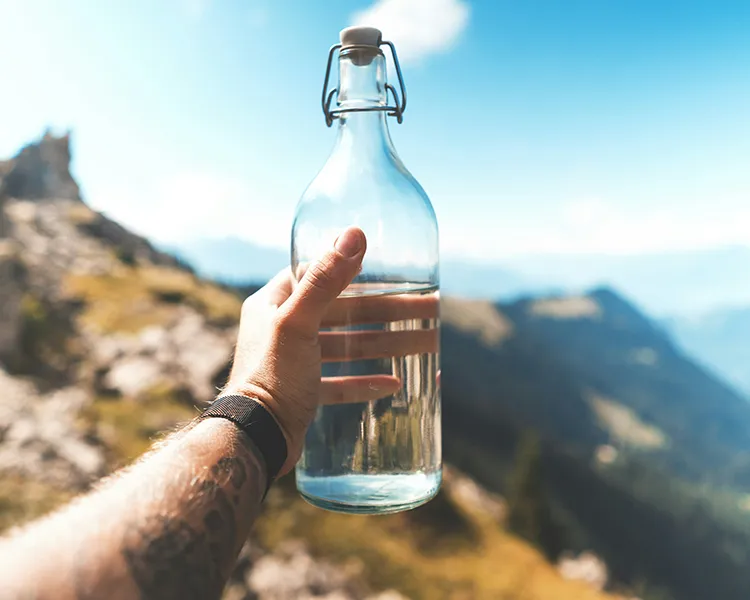Mano sostiene botella con agua frente a monta&ntilde;as y cielo azul