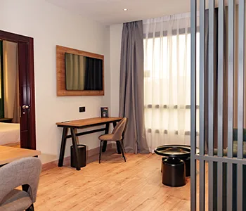 Estancia de hotel con mesa, sillas y cortinas junto a una mampara.