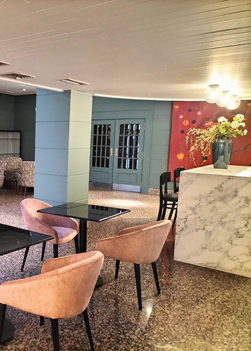 Interior de cafeter&iacute;a con mesas, sillas y barra de m&aacute;rmol, estilo moderno.