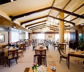 Comedor con mesas y sillas bajo techo de madera y l&aacute;mparas colgantes.