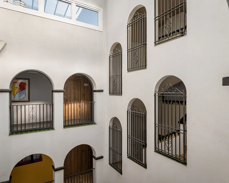 Patio interior con muros blancos y varias ventanas con rejas met&aacute;licas