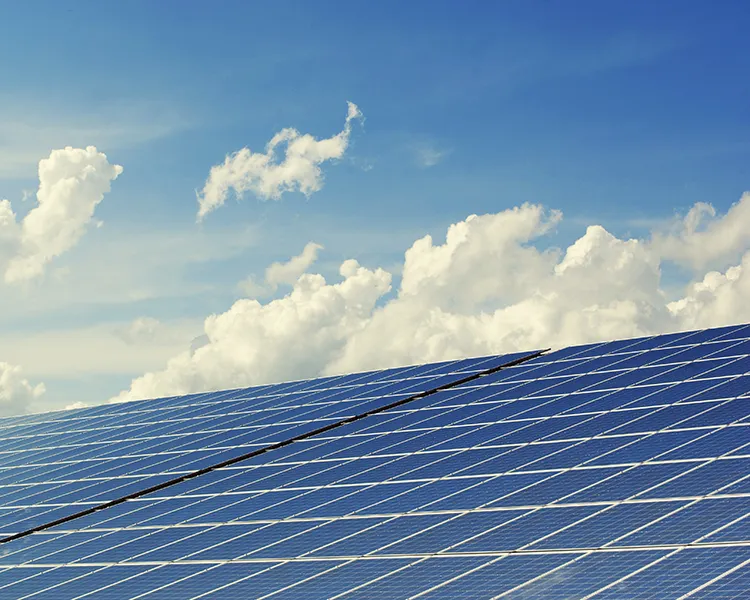 Paneles solares azules sobre cielo azul con nubes blancas.
