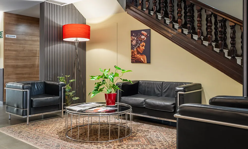Sala de estar moderna con sof&aacute; negro, mesa redonda y l&aacute;mpara roja bajo escalera