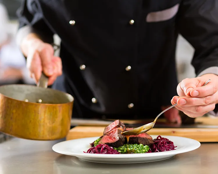 Chef sirve plato con carne, verduras y pur&eacute; de remolacha en plato blanco