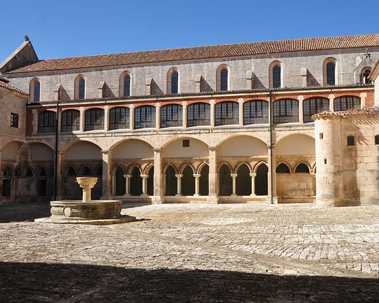 Patio de piedra con arcos y fuente en un claustro hist&oacute;rico.