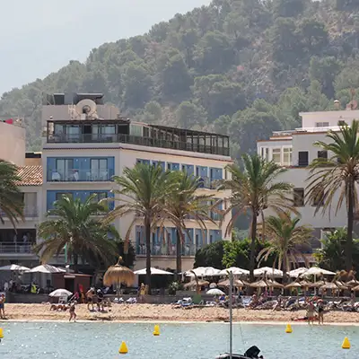 Hotel junto a la playa con palmeras y sombrillas sobre arena y mar.