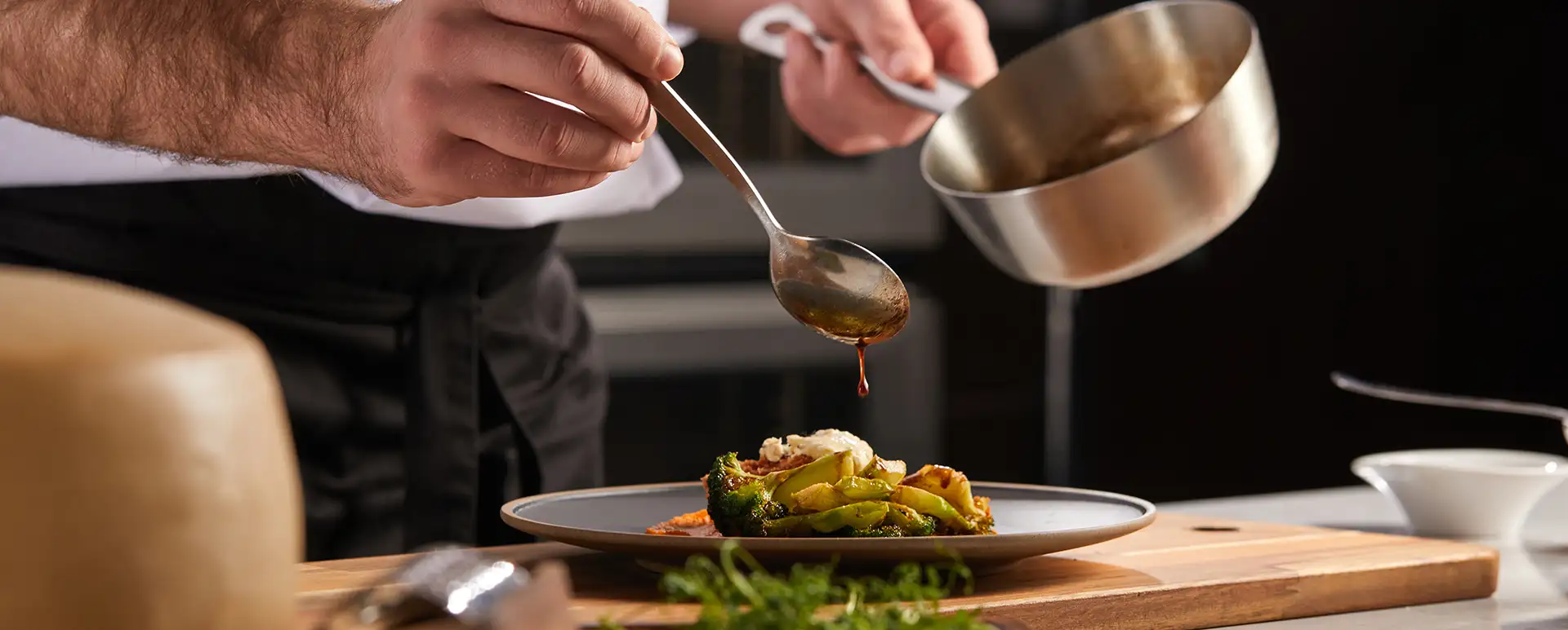 Mano de chef sirve salsa con cuchara sobre plato con verduras y pollo