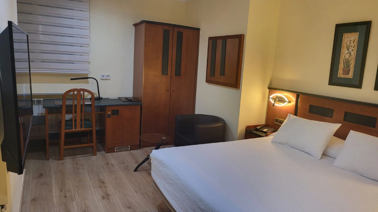 Habitaci&oacute;n de hotel con cama doble, sill&oacute;n, escritorio, armario y ventana