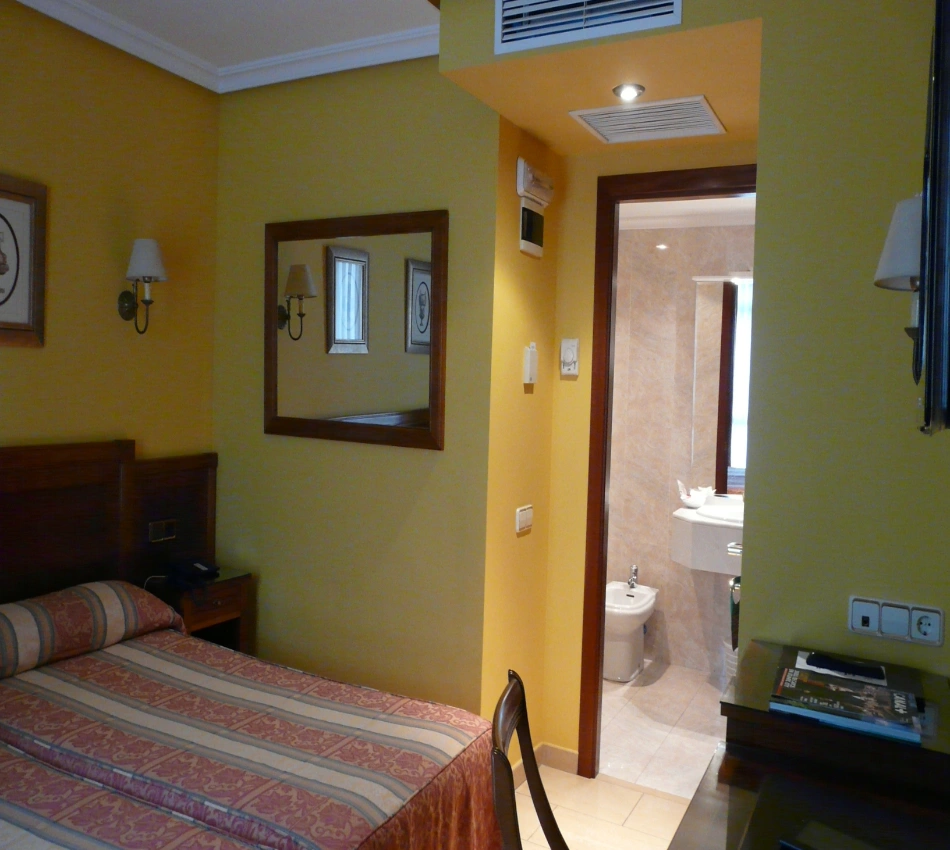 Dormitorio con cama, espejos y ba&ntilde;o al fondo, luces empotradas.