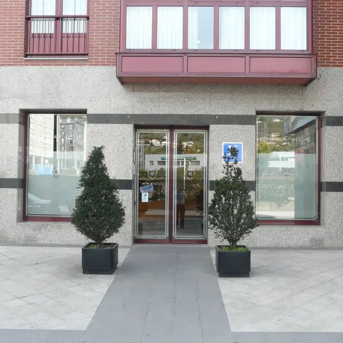 Entrada de edificio con puerta doble de vidrio y dos macetas.