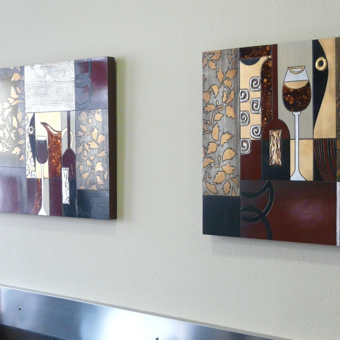 Cuadros decorativos con copas y botellas sobre pared blanca.