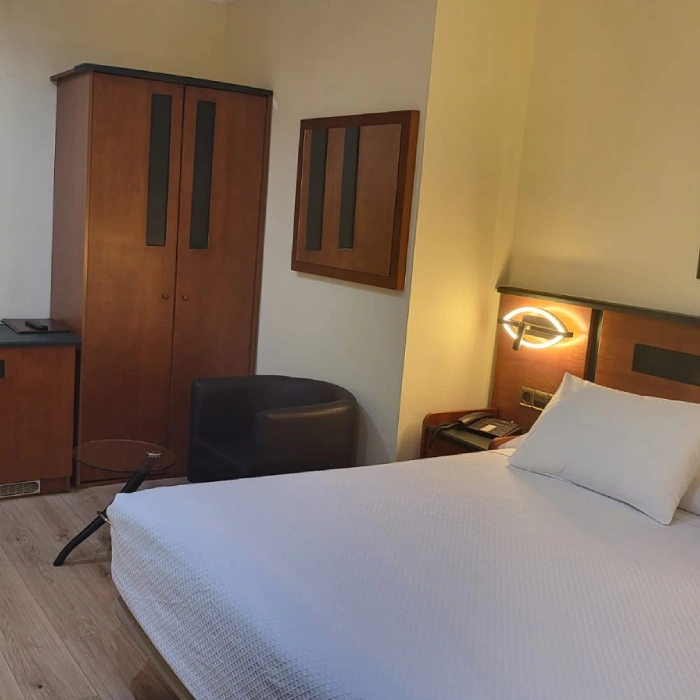 Habitaci&oacute;n de hotel con cama doble, sill&oacute;n y armario de madera.