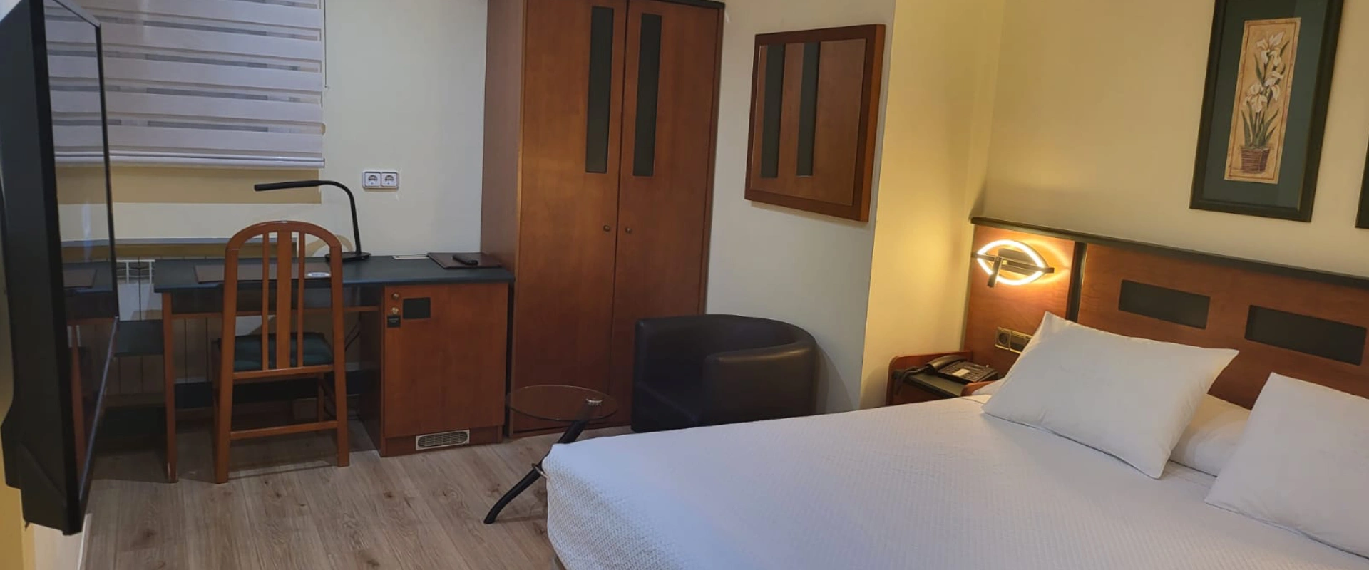 Habitaci&oacute;n de hotel con cama doble, sill&oacute;n y escritorio cerca de una l&aacute;mpara.